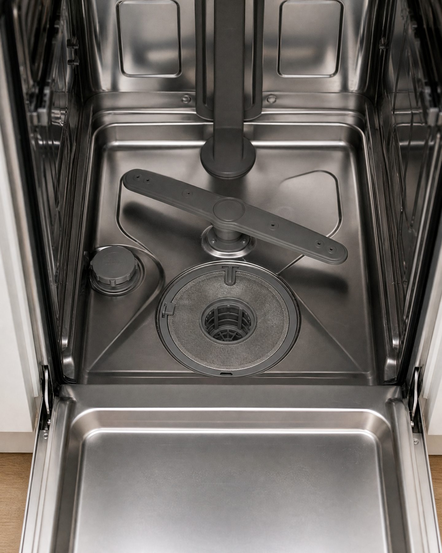 top-down view of dishwasher interior with lower rack removed showing circular filter near spray arm
