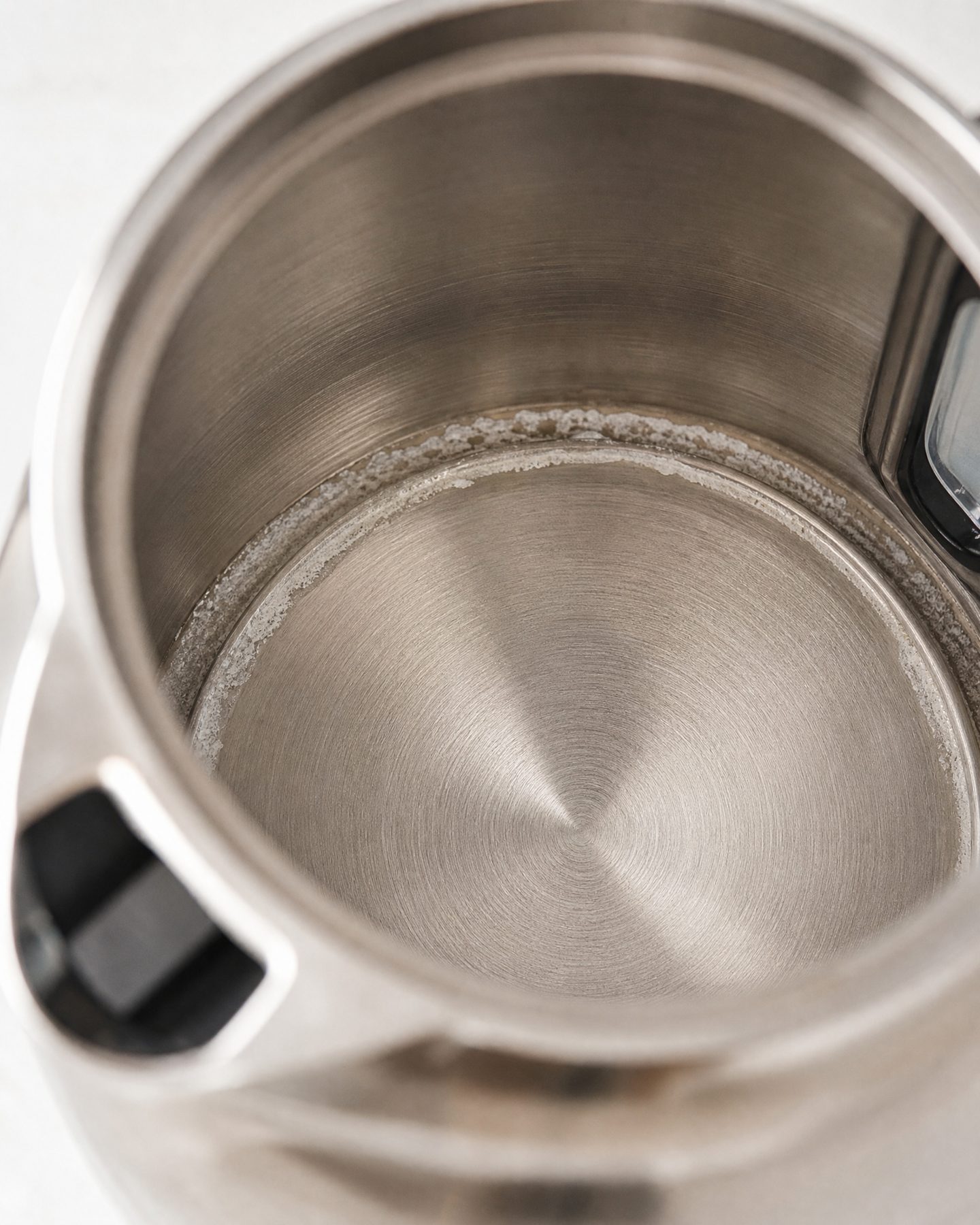 close-up of white chalky mineral scale inside an unplugged stainless electric kettle